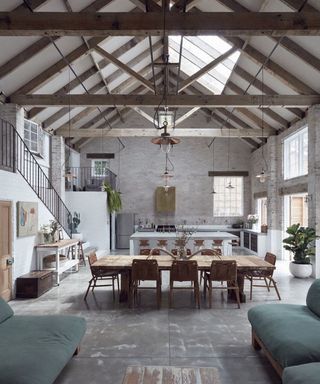 A grey industrial open-plan home with green sofas in living room, dining table and lots of layered lighting