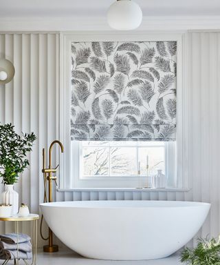 Simple monochrome patterned roman blind over window in bathroom with large white freestanding bath tub