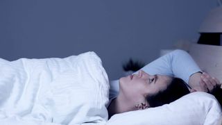 A woman lies in bed, staring up at the ceiling, unable to sleep