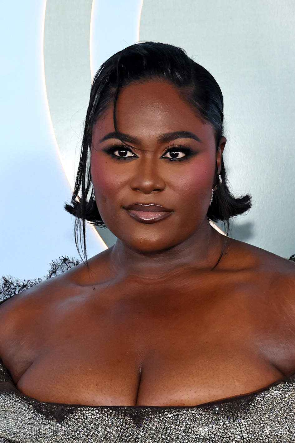 a black woman with dark hair wears dark eye makeup and a ponytail at a red carpet event