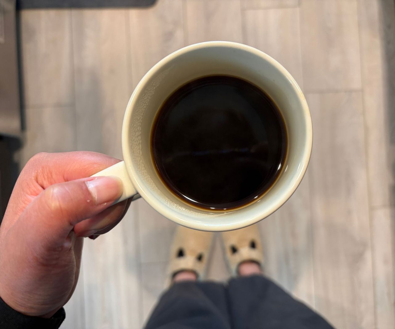 A mug of black coffee viewed from above, being held by someone.