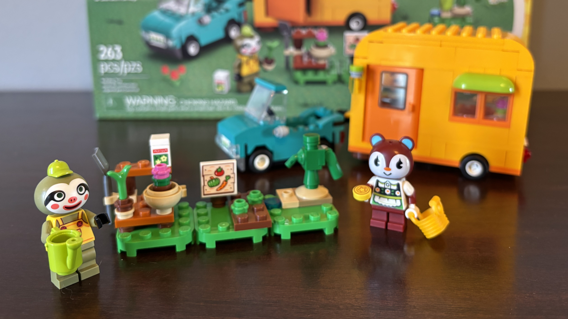 Lego Leif&#039;s Caravan &amp; Garden Shop character minifigures, box, and vehicles on a wooden surface