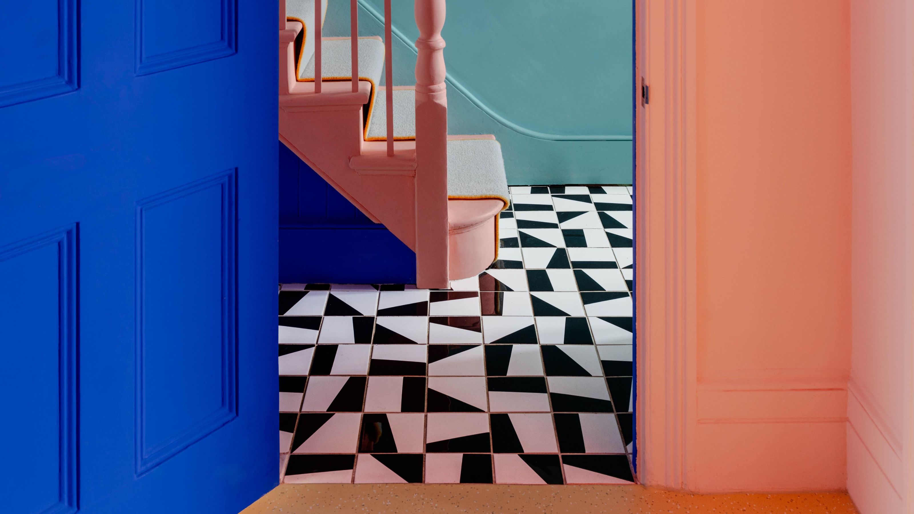 a view through into a hallway with black and white floor tiles, the space is painted in light pink and cobalt blue