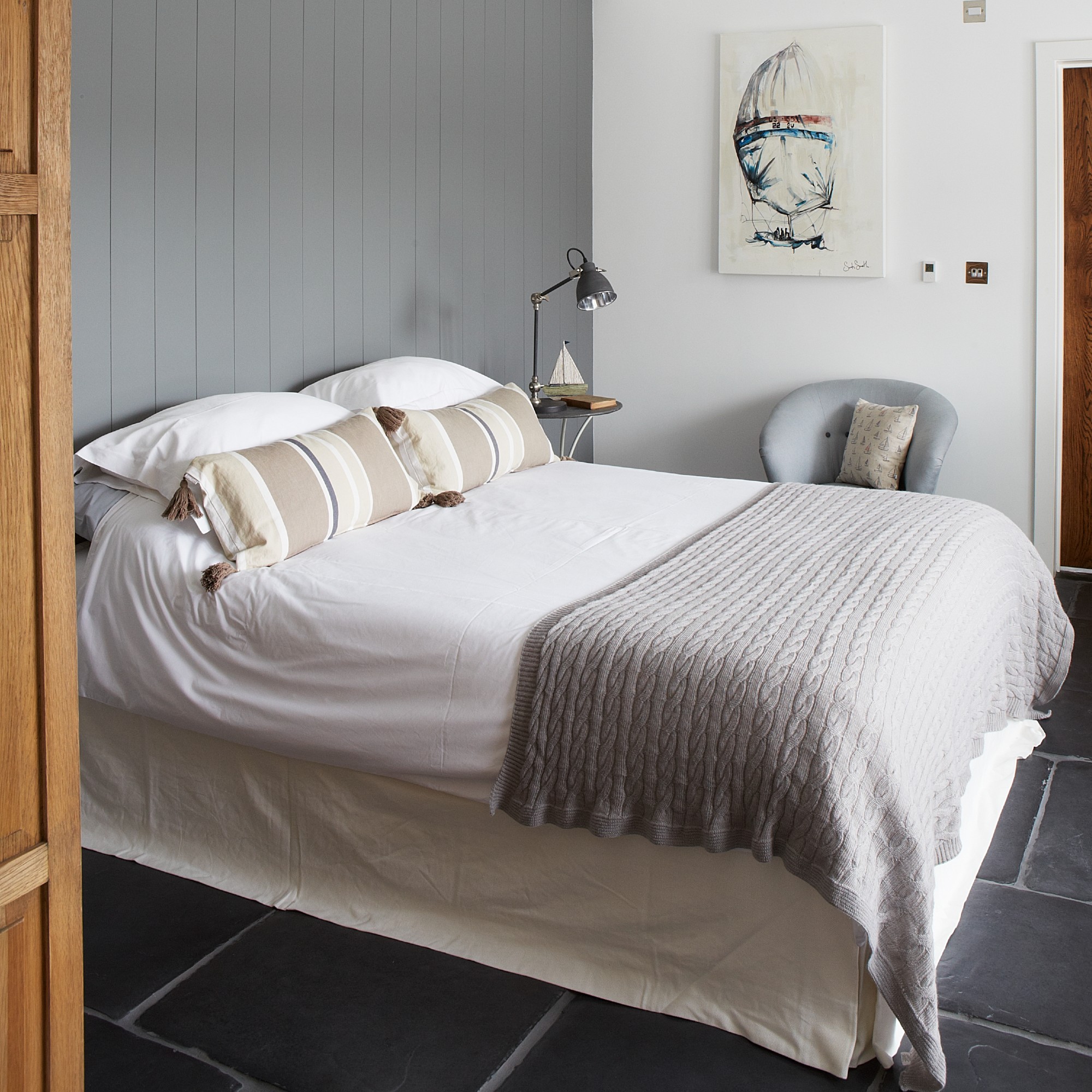 A small bedroom with the bed dressed in white bedding with a matching valance and set against a feature grey panelled wall