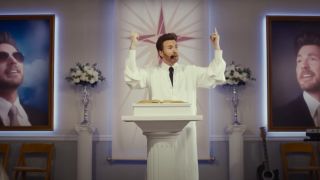 Chris Evans in Honey Don't! preaching to a room full of people enthusiastically behind a podium in a headset.