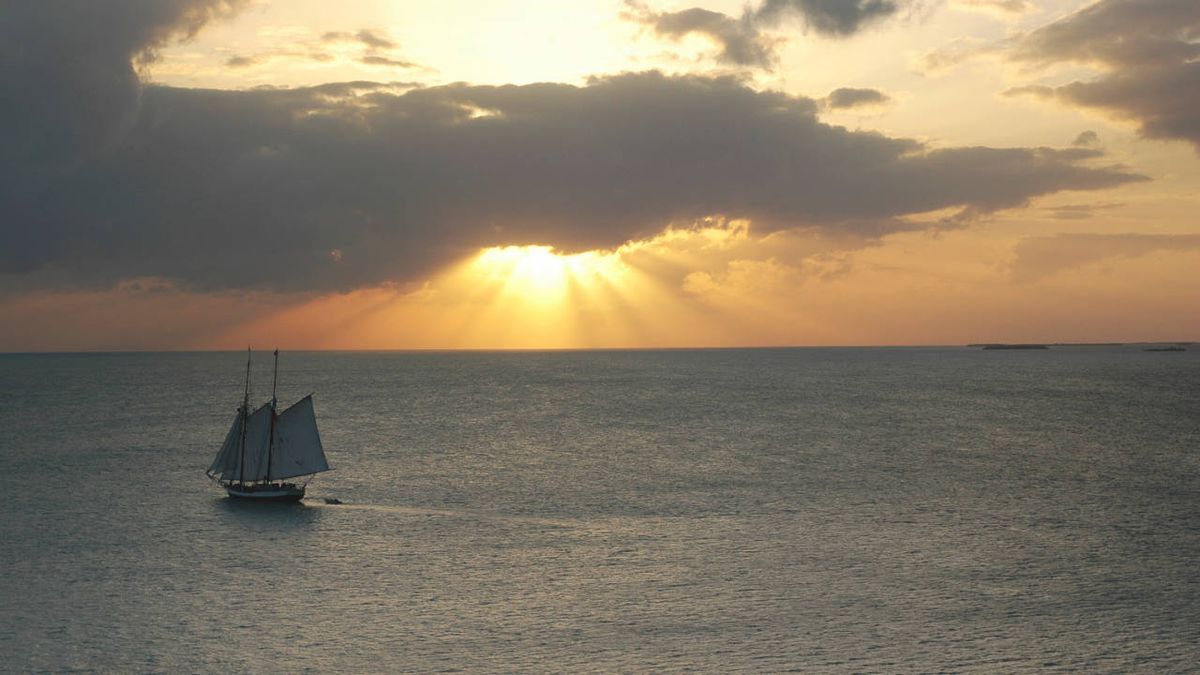 Old fashioned sailing vessel on the sea, with setting sun on the horizon