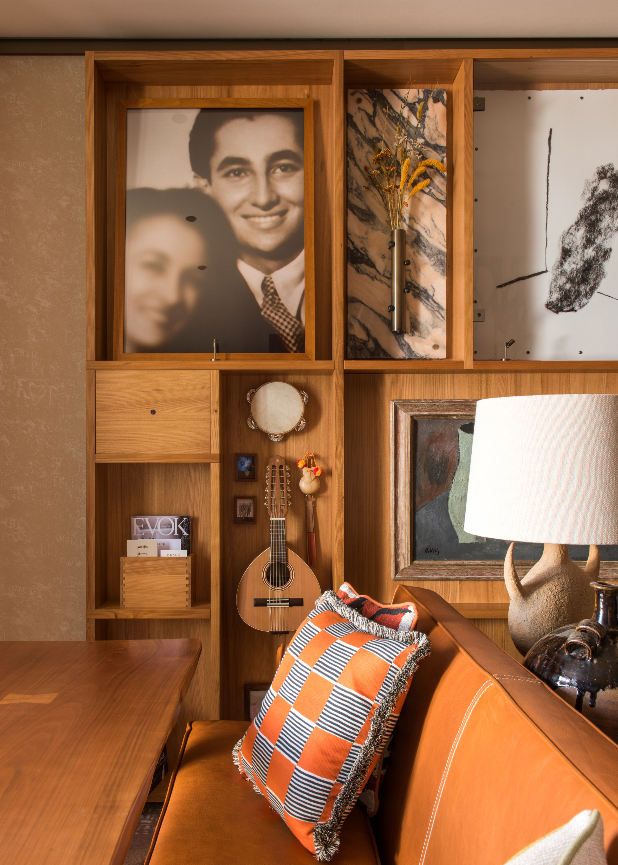 A wood wall unit with marble decorative accents and musical instruments alongside art in front of a sofa with colorful pillows