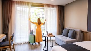 A woman opening up the curtains in a hotel room