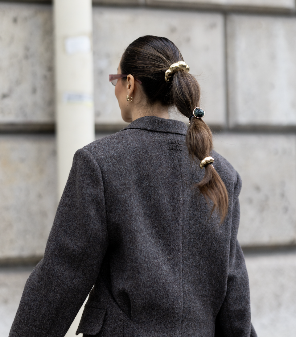 A woman wearing hair cuffs with gold detailing around her ponytail. She is also wearing a grey blazer.