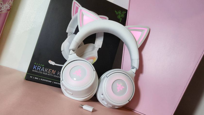 Photo of the white Kraken Kitty V3 Pro headset leaning against its box and a pink desk bookshelf.
