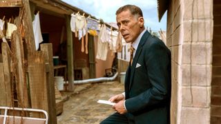 Benny in a suit standing in the slum housing he owns