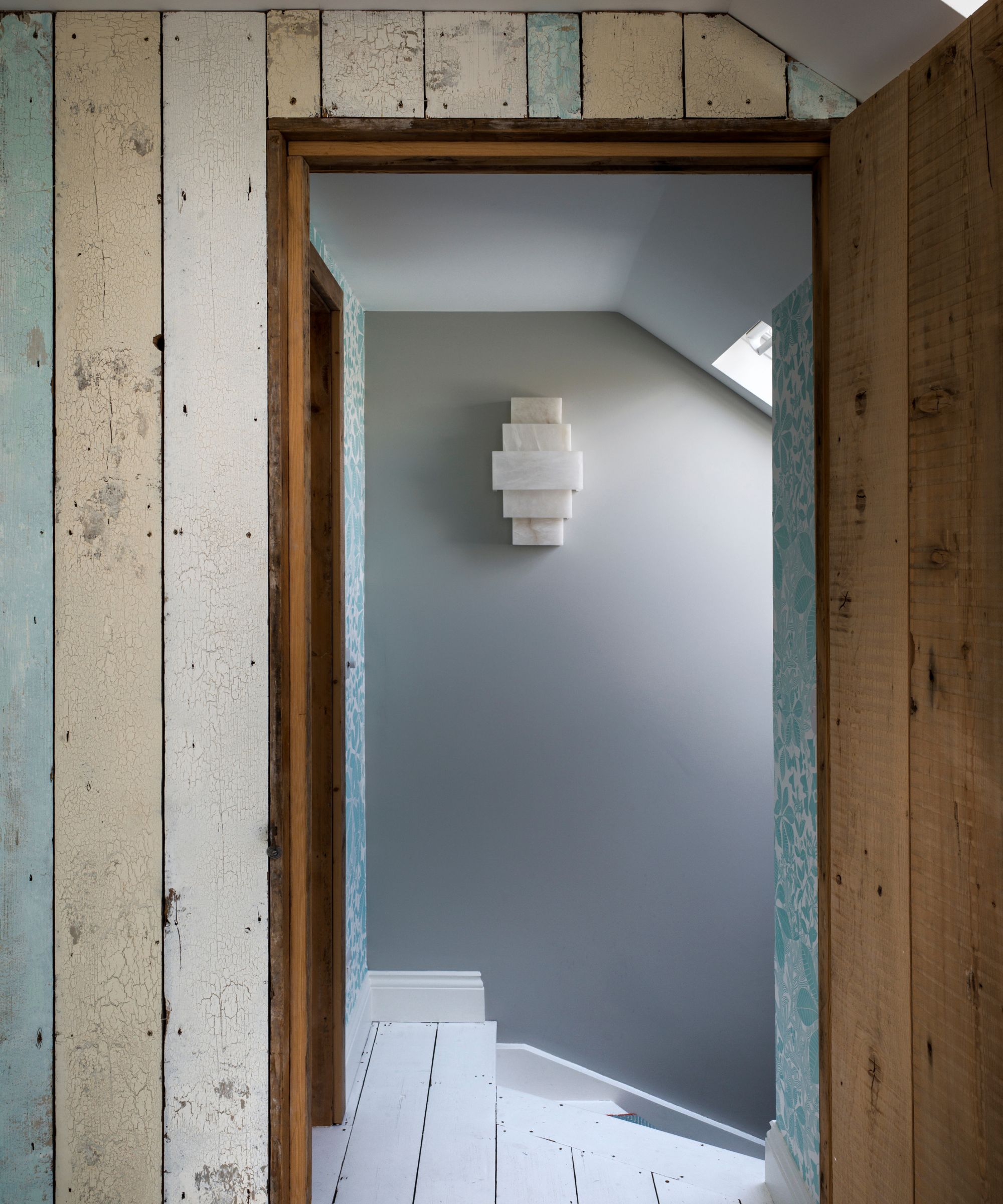 A wood panelled attic space with blue, beige and white colors and a white marble statement light fixture on the wall