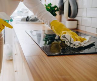 Someone cleaning a a glass stove top with a sponge and soap