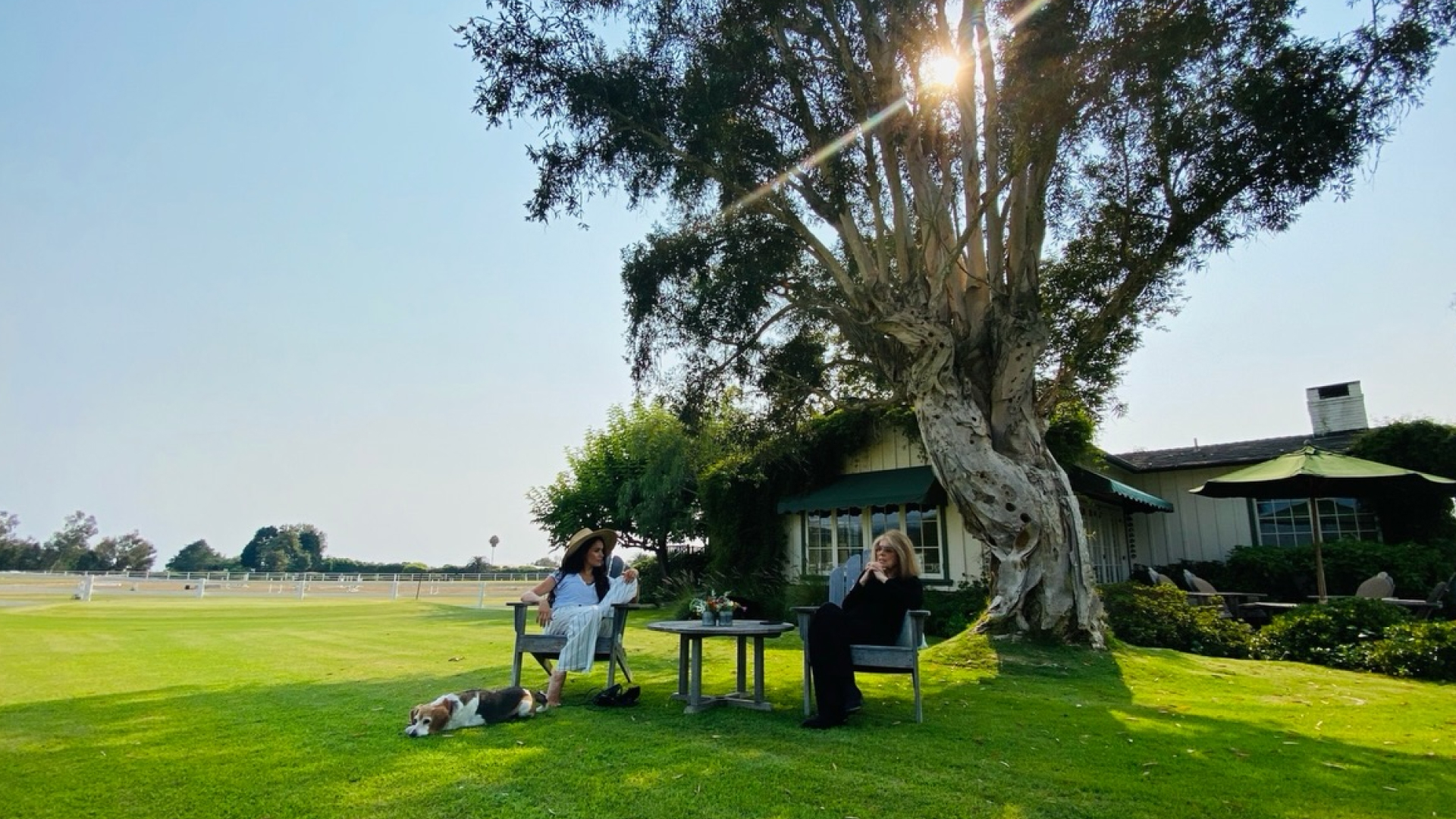 Meghan Markle and Gloria Steinem sitting on chairs in front of a house and tree 