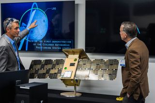 Jeffrey Parker (left), chief technology officer of Advanced Space, explains the CAPSTONE mission to Sen. John Hickenlooper (D-Colo.) using a full-size model of the spacecraft.