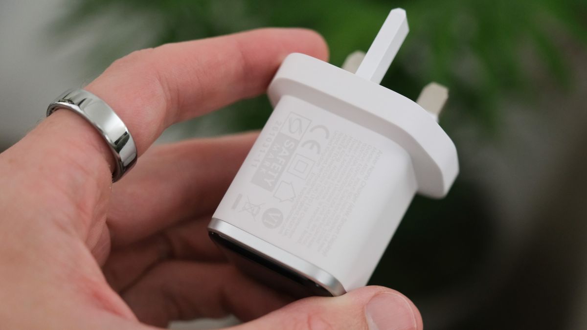 Close-up of the white Anker Nano Charger held in a hand, showing its UK three-pin plug and regulatory markings.