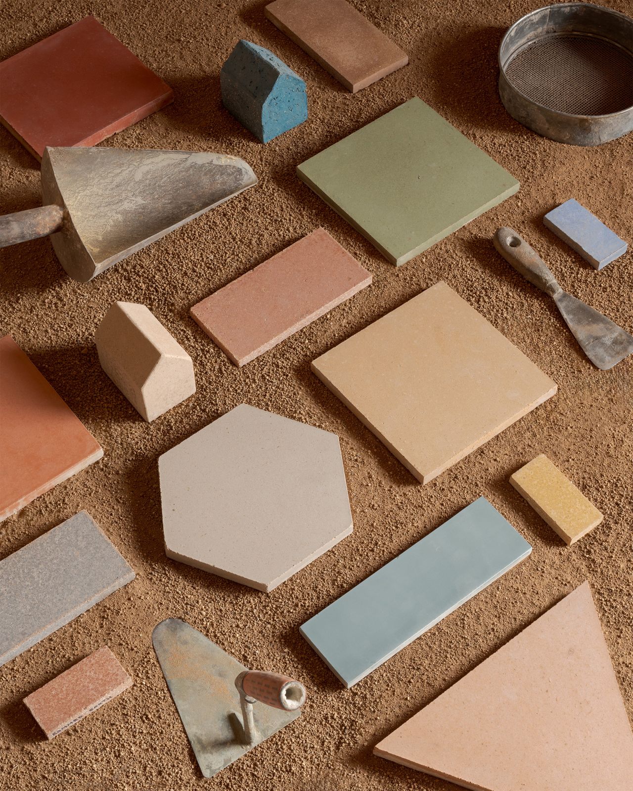 A series of colorful tiles in pastel shades, placed atop an earthy surface alongside utensils.