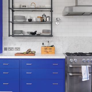 Kitchen with dark parquet flooring, bright blue kitchen cupboards and white worktop and tiled walls