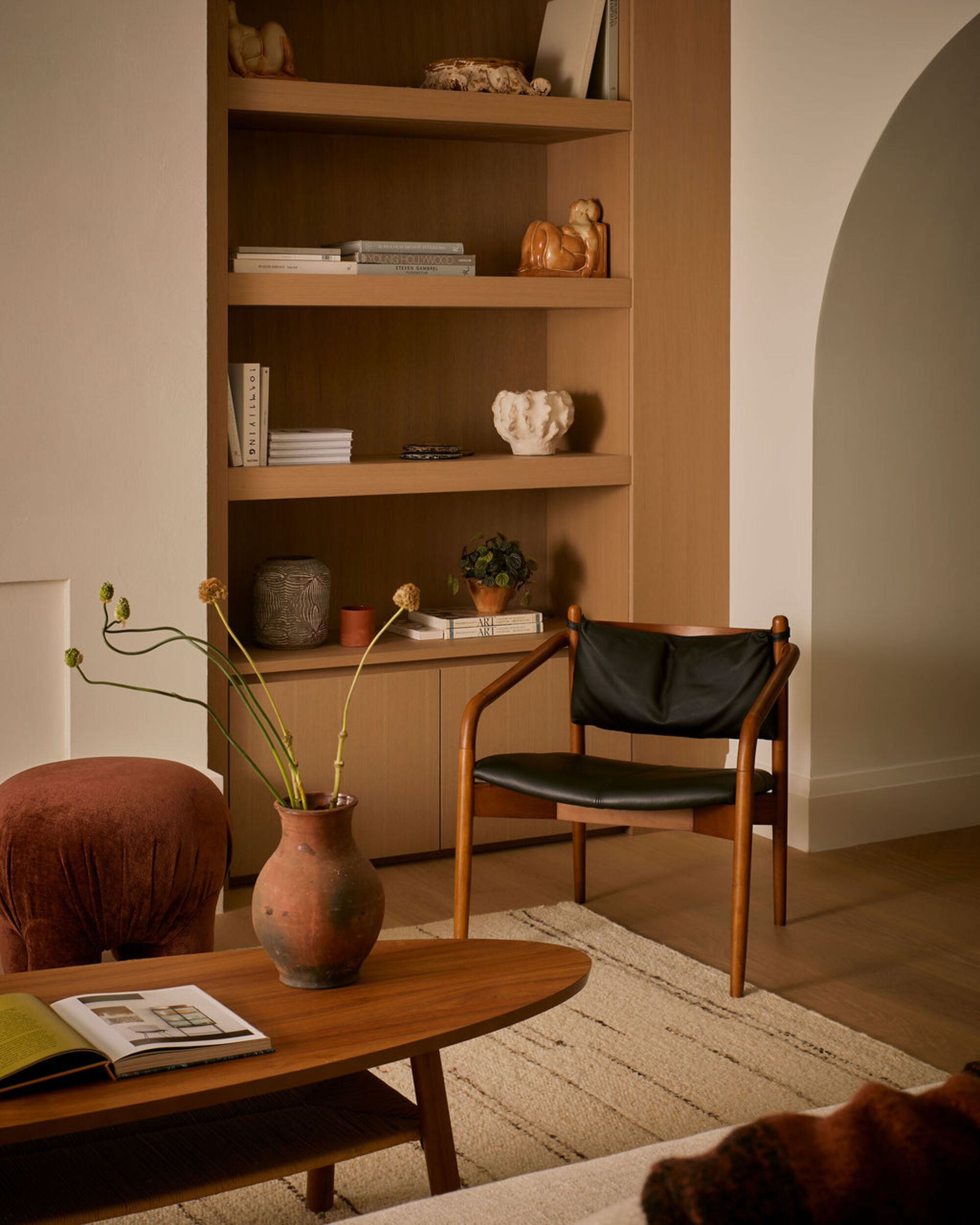 a living room with a built-in timber bookshelf, leather chair and oval timber coffee table