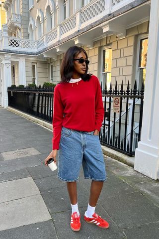 a photo showing what colors go with red, specifically a woman wearing a red sweater with blue denim shorts and red sneakers