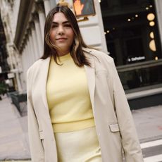 Woman standing on New York City street wearing beige blazer, yellow vest, and yellow maxi skirt.