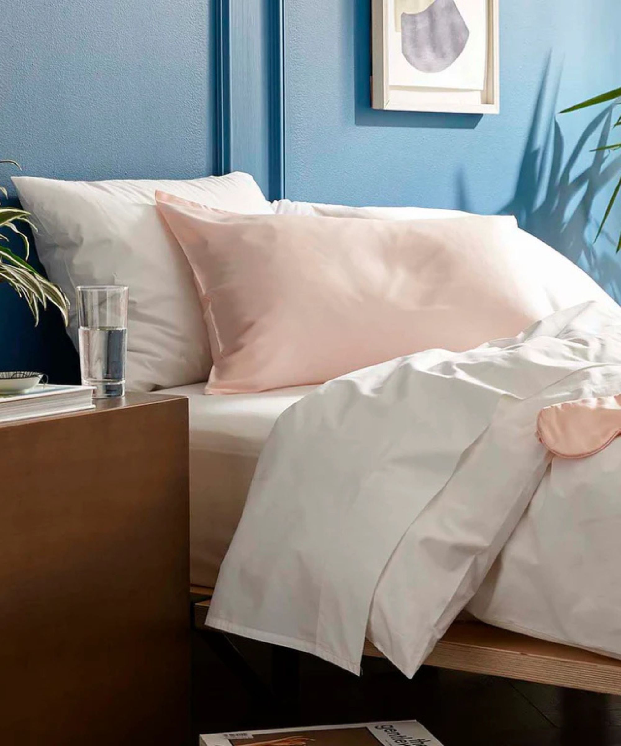 Bed with white sheets and a pink silk pillowcase with a matching sleep mask