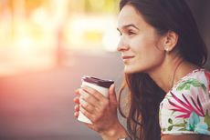 A woman drinks a cup of coffee and looks happy