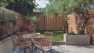 A small garden with round table and lawn with wooden fence panel boundary