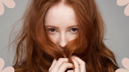 A shot of a woman with long red, healthy hair, holding it over her face to illustrate how bond builders for hair can boost hair health