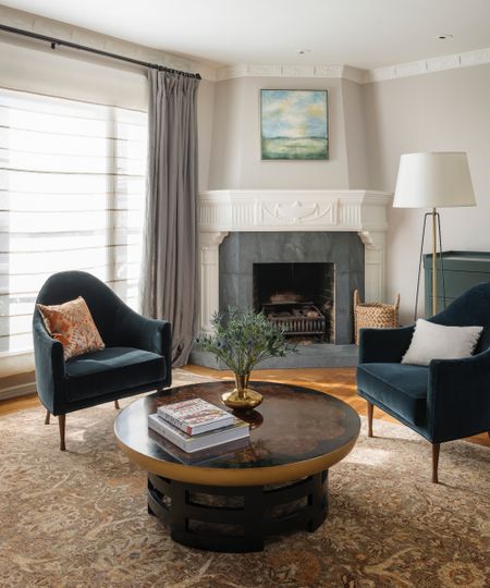 Slate traditional fireplace in lounge with dark teal fabric chairs, round wooden coffee table and Persian style area rug