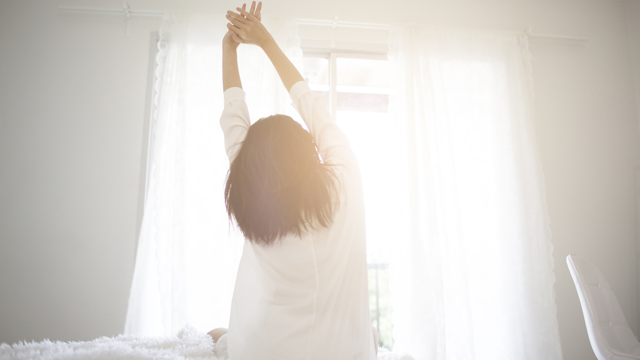 A woman in a white shirt sits on her bed to stretch