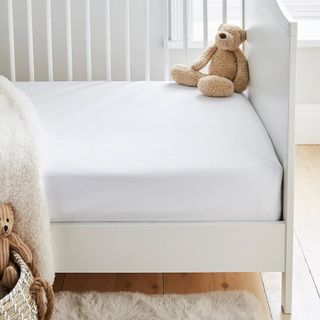 A white kids bed with a teddy bear sat in one corner