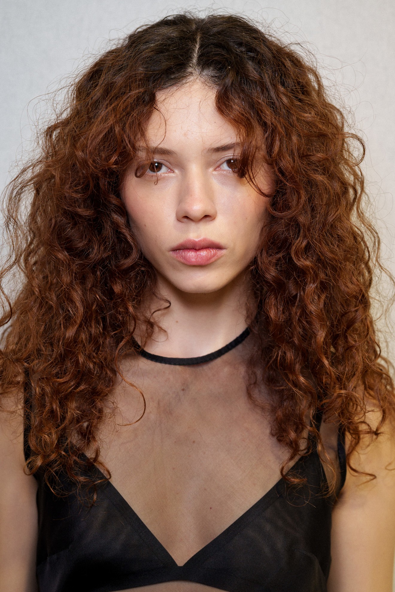 A model showing off their natural hair texture with a red tint and a black sheer top