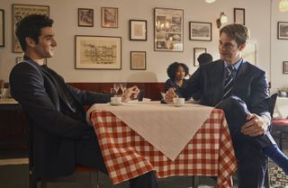 two men (Taylor Zakhar Perez as Alex Claremont-Diaz and Nicholas Galitzine as Prince Henry) gaze at each other while sitting at a restaurant table, in the Prime Video rom-com 'Red White and Royal Blue'