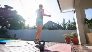 Woman using skipping rope on yoga mat in back garden at home