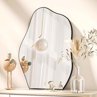 Abstract mirror with black edges, placed on a light wooden shelf, leaning against a beige wall