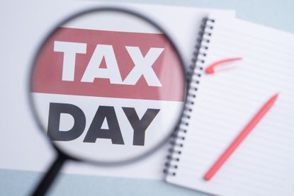 magnifying glass with "Tax Day" printed underneath, beside a pen and spiral notebook