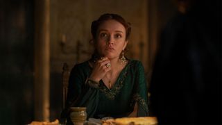 Queen Alicent Hightower (Olivia Cooke) looks pensive with her elbows leaning on a desk