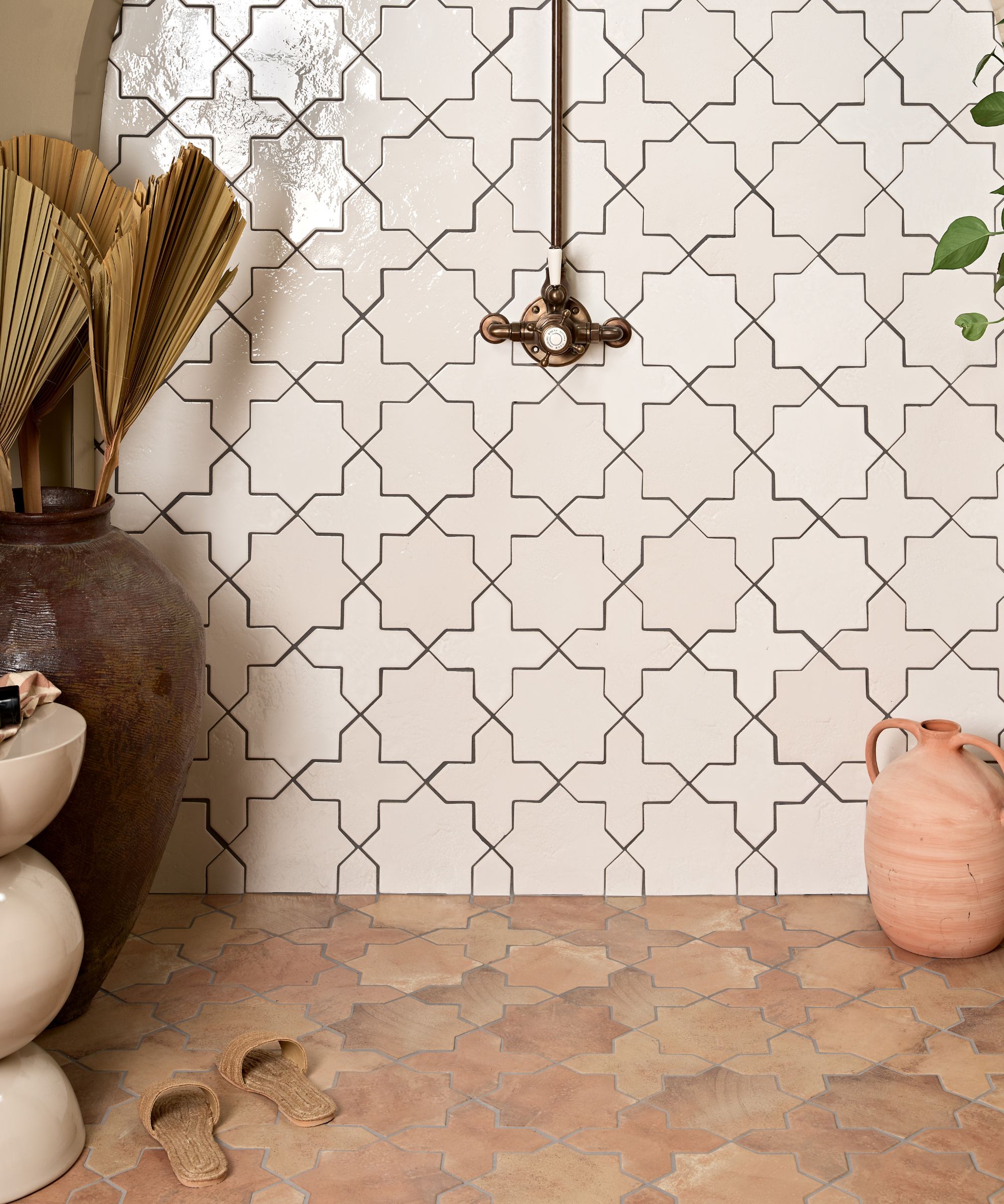 A shower with white geometric tiles on the wall and terracotta geometric tiles on the floor
