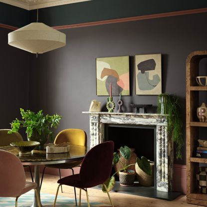 A dining room with a marble fireplace and a round dining table painted in Benjamin Moore's Silhouette shade, a dark brown with a charcoal undertone with a teal panel at the top