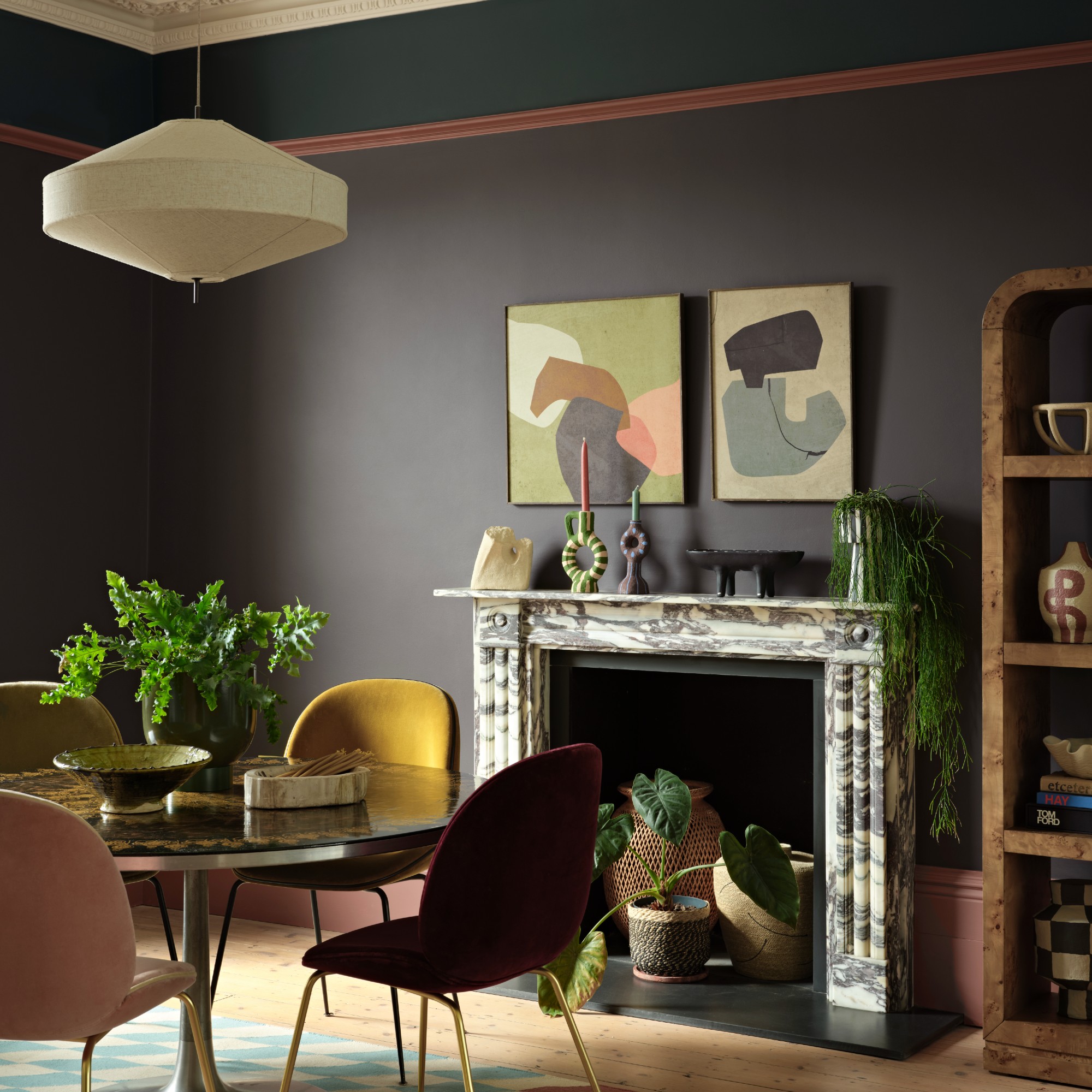 A dining room with a marble fireplace and a round dining table painted in Benjamin Moore&#039;s Silhouette shade, a dark brown with a charcoal undertone with a teal panel at the top