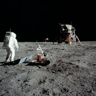 astronauts in bulky spacesuits walk on the grey dusty surface of the moon