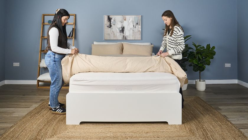 Two female testers change the bedding of a bed in a blue bedroom. 