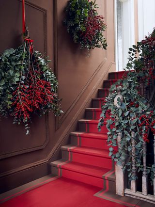 Christmas stair decor with large eucalyptus garland and bouquets in red hallway by Annie Sloan