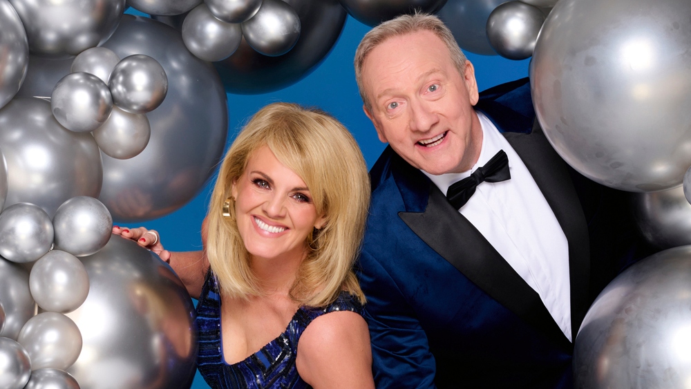 Sally Lindsay and Neil Dudgeon in smart clothing and posing with silver balloons for the TV Times 70th birthday cover shoot 