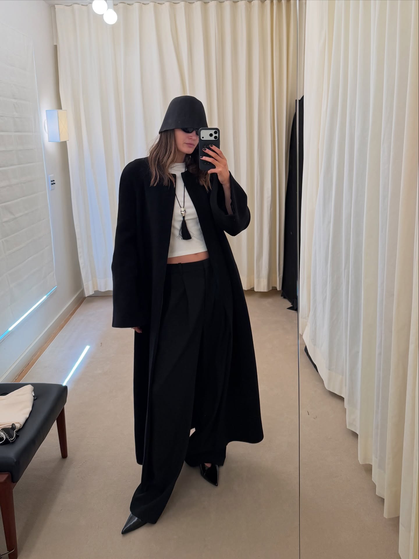 An image of @cocoschiffer wearing a white cropped t-shirt, black trousers, black wool coat, black wool bucket hat and a tassel necklace.