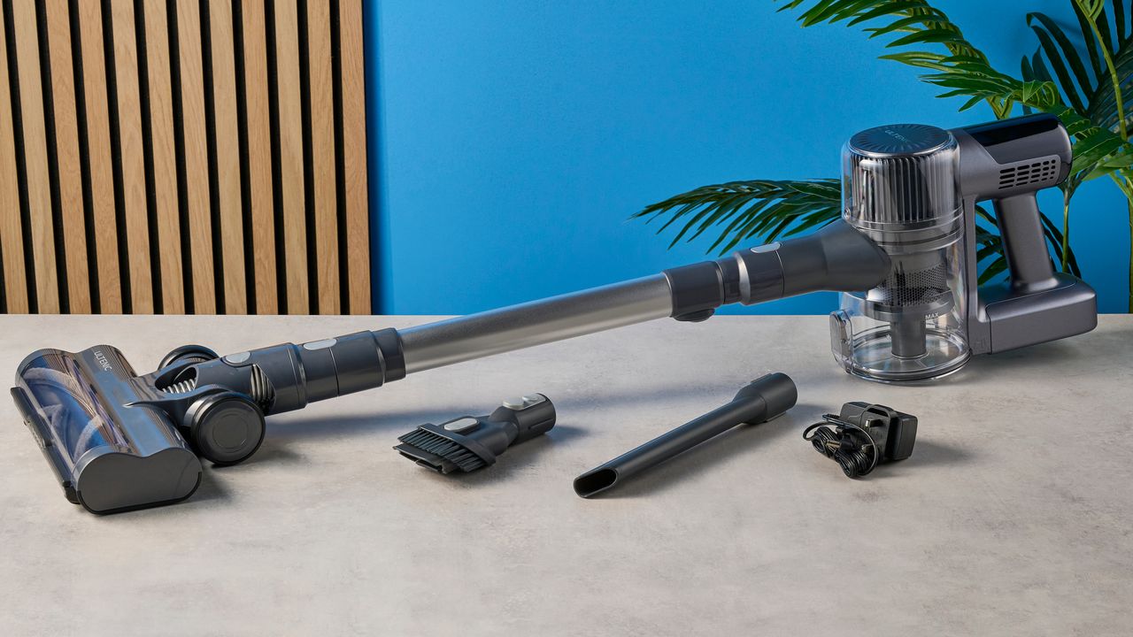 a closeup shot of the brush and crevice component tools of a modern-looking sleek shiny vacuum cleaner with light grey components on a carpet in front of a blue background