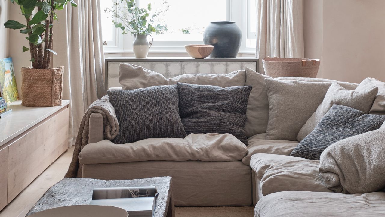 A living room with a slouchy beige corner sofa and contrasting grey cushions