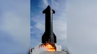 a sleek black rocket fires its engines while stationary on a launch pad