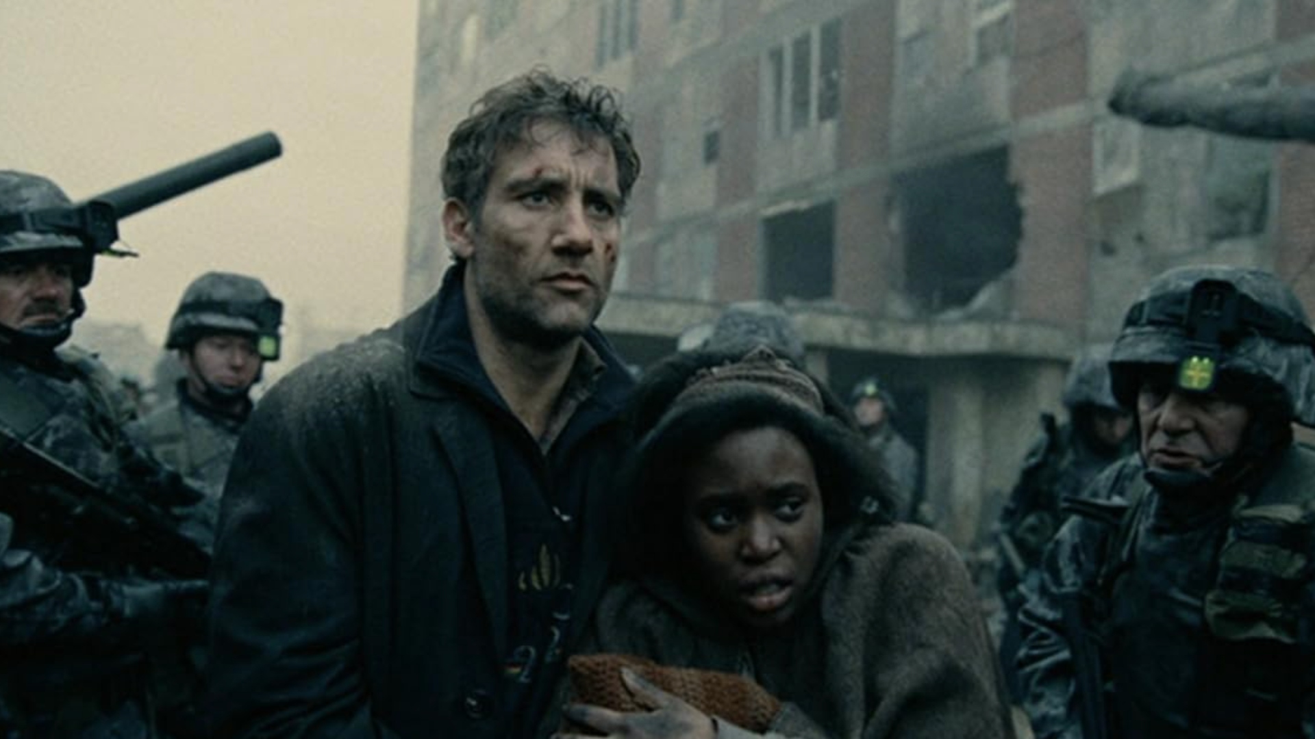 A woman huddles close into a man who has rugged clothes and scuffed clothes are surrounded by soldiers, tanks and a crumbling building